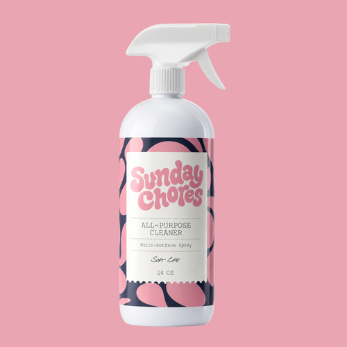 A 24 oz spray bottle of Sunday Chores All-Purpose Cleaner in 'Soft Love' scent, featuring a white bottle and trigger sprayer with a pink and dark patterned label, set against a solid pink background.